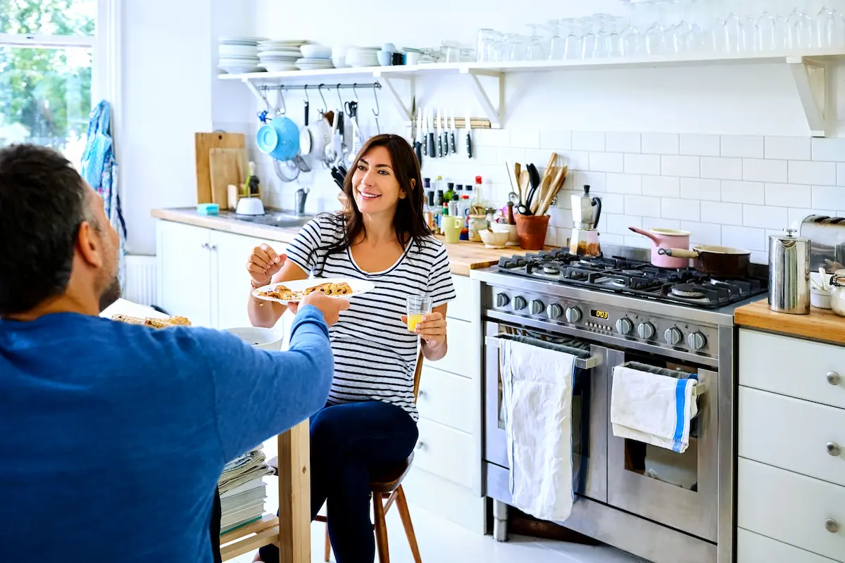 Man and woman sitting at kitchen table with cooking range in the background 